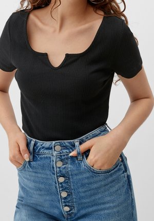 Sort ribstrikket top med rund udskæring og korte ærmer, kombineret med højtaljede, knapgylp lyseblå denimjeans.