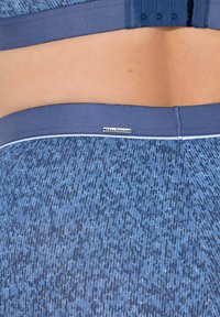 Texturované modré legíny s jemným geometrickým vzorem. Mají hladký, elastický pás. Viditelná kovová logo nášivka na zadní straně.