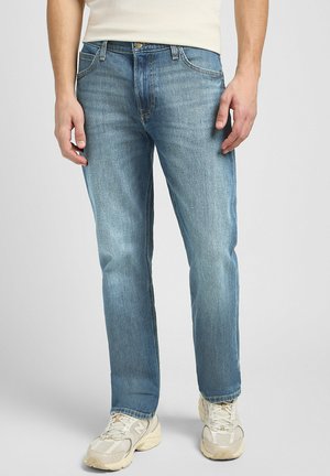 Ljust blå denimjeans med rak passform, med stickade fickor och en subtil blekt textur. Matchas med beiga sneakers.