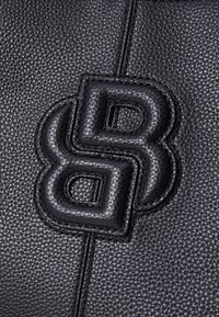 Sac en cuir noir avec une surface texturée et un logo en relief bien visible, offrant un contraste de matière lisse.