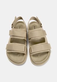 Beige szandál három állítható textil pánttal, nyitott orrú dizájn, párnázott talpbetéttel és texturált talppal. Könnyű kivitel.