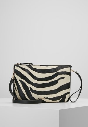 Sac bandoulière rectangulaire avec rayures zébrées noires et blanches, une bandoulière noire réglable et des éléments métalliques dorés, posé sur une surface blanche.