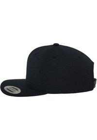 Casquette snapback noire avec visière plate et bride ajustable vue de profil gauche sur fond blanc.