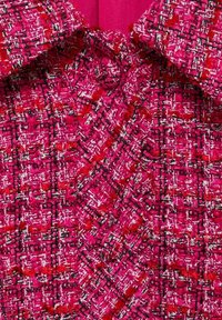 Teksturowana różowa tkanina tweedowa w wzór houndstooth, z czerwonymi i czarnymi akcentami. Kołnierz jest wyraźnie widoczny na górze.