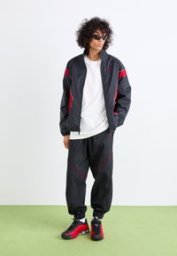 Black windbreaker with red accents, white t-shirt, and black pants featuring red stitching, paired with red and black athletic shoes.
