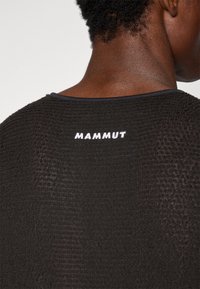 Cămașă neagră cu textură, cu decolteu rotund. Prezintă un logo alb "MAMMUT" pe spate. Materialul are un model țesut și o strălucire ușoară.