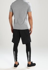 Harmaa lyhythihainen paita, mustat shortsit ja mustat legginssit, joissa on valkoista brändäystä ja teksturoitu sivukuosi, yhdistettynä mustiin urheilukenkiin.