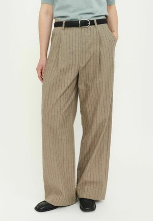 Beżowe spodnie o szerokich nogawkach z pionowymi paskami, wykonane z teksturowanej tkaniny. Z dodatkiem czarnego paska i bocznych kieszeni. Obuwie to czarne mokasyny.