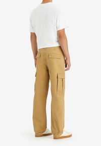 Khaki spodnie cargo o luźnym kroju, z bocznymi kieszeniami i kieszeniami z klapką z tyłu. Połączone z białą koszulką i sneakersami.