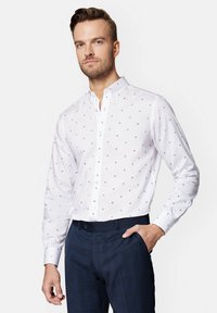 Biała koszula w małe szare kropki, z kołnierzykiem zapinanym na guziki i długimi rękawami, zestawiona z granatowymi spodniami w kratkę. Gładka tekstura materiału.