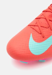 Bright coral soccer cleat featuring textured synthetic material, pink accents, and a distinct light blue Nike swoosh on the side.