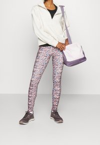 Polarowy sweter w kolorze kremowym, zestawiony z wielokolorowymi legginsami w kwiaty oraz torbą w kolorze fioletowym i różowym. Szare buty sportowe dopełniają stylizację.