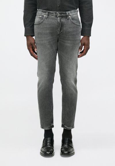 Jeans en denim gris avec une coupe slim, design à cinq poches, texture décolorée et légères traces d'usure, associés à des mocassins noirs et des chaussettes.