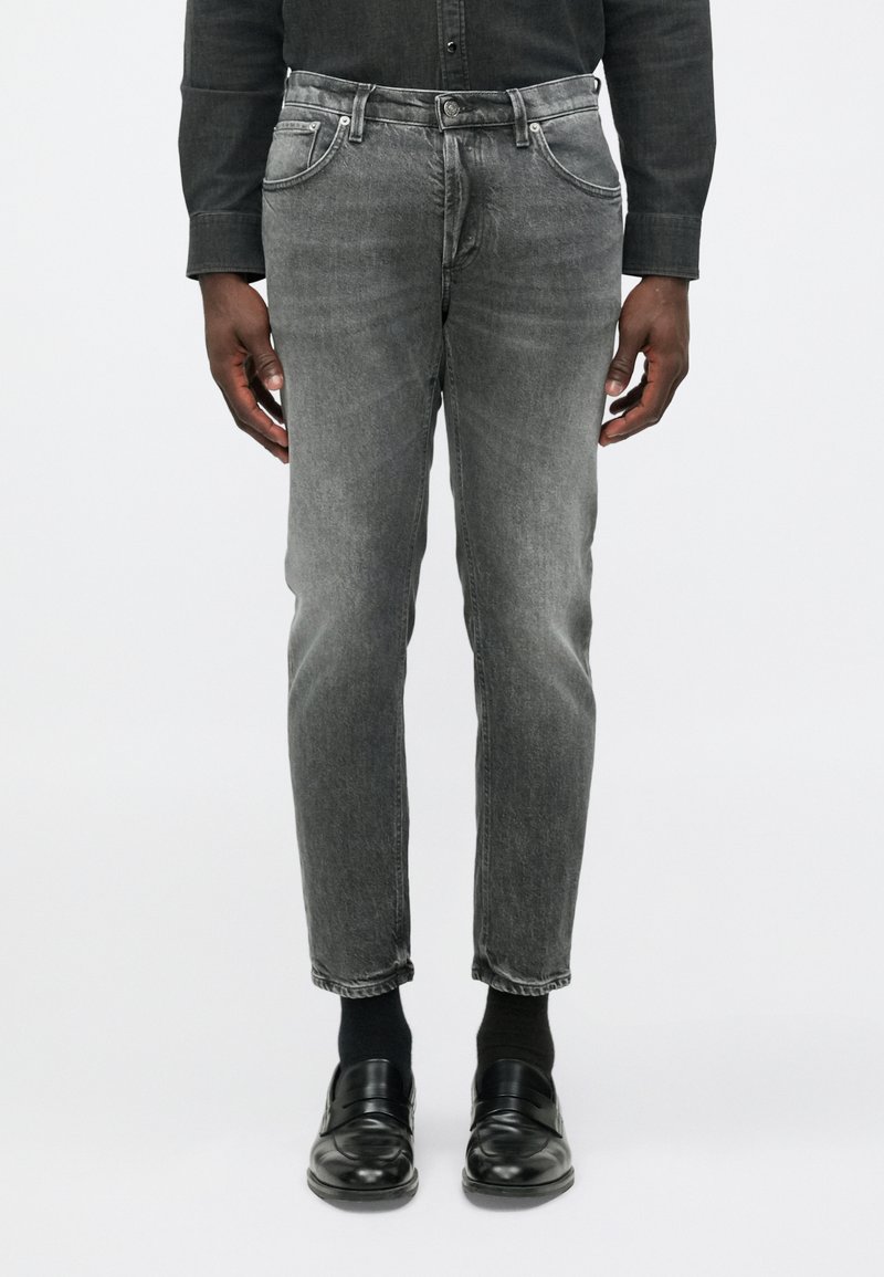 Jeans in denim grigio con una vestibilità slim, design a cinque tasche, texture sbiadita e leggere sfumature, abbinati a mocassini neri e calze.