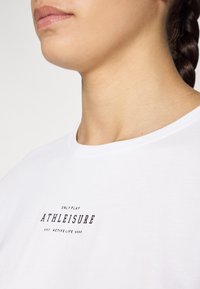 Tricou alb cu guler rotund, textură moale, cu inscripția imprimată „ONLY PLAY ATHLEISURE EST. ACTIVE LIFE 2006” în negru.