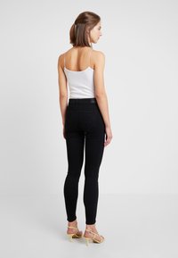 Høyt liv svarte jeans med en slank passform, diskret søm og baklommer, kombinert med en hvit tanktopp og gule hælsandaler.
