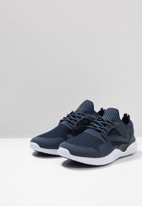 Sneakers atletiche di colore blu navy con tomaia in maglia testurizzata, dettagli neri e suola bianca. Presentano un design con lacci e colletto imbottito alla caviglia.