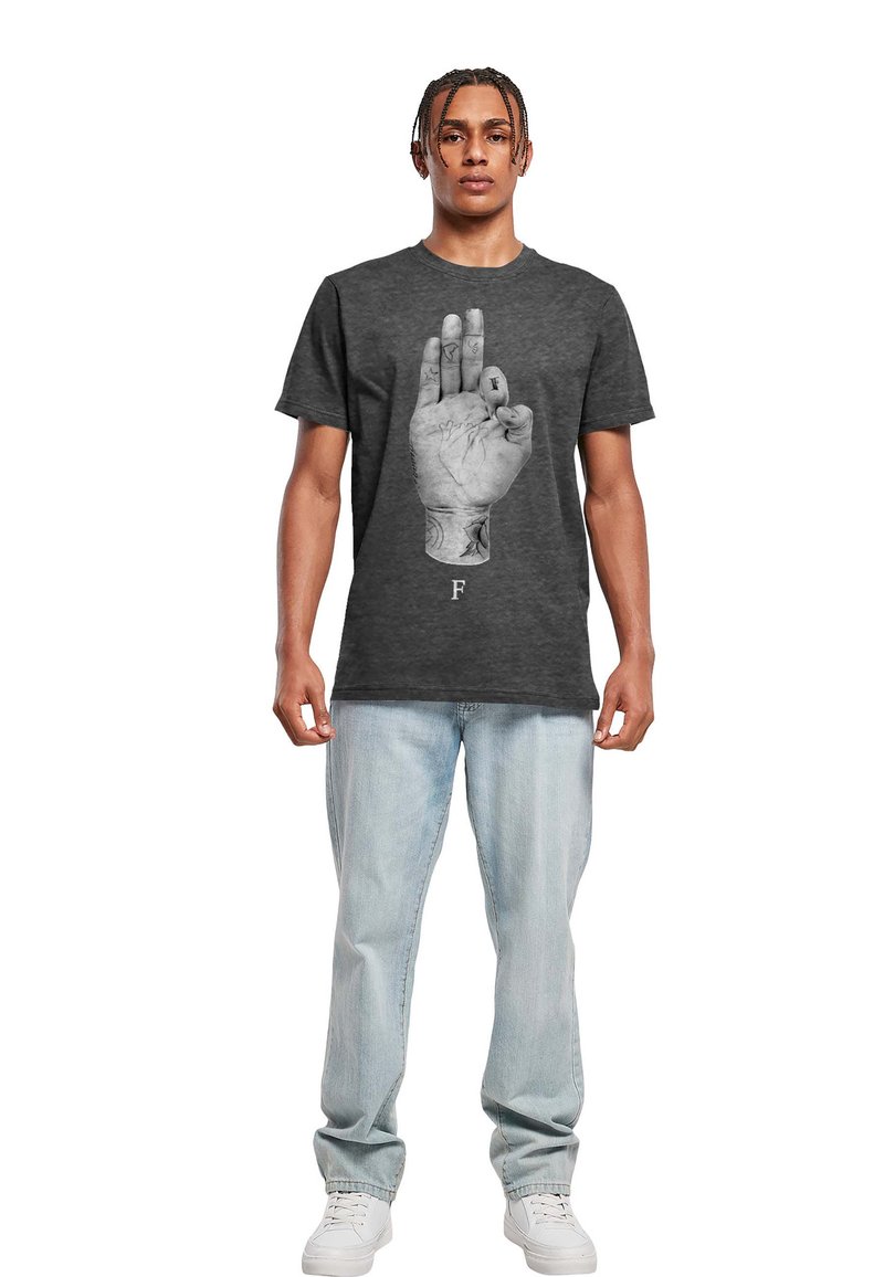 Grå t-skjorte med korte ermer som viser et detaljert grafisk motiv av en hånd med tatoveringer, vist på en mannlig modell i kombinasjon med lys blå jeans.