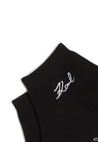 Melni potītes zābaciņi ar baltu izšūtu "Karl" logo tuvumā pie apakšmalas, redzama teksturēta auduma un elastīga ribbinga.