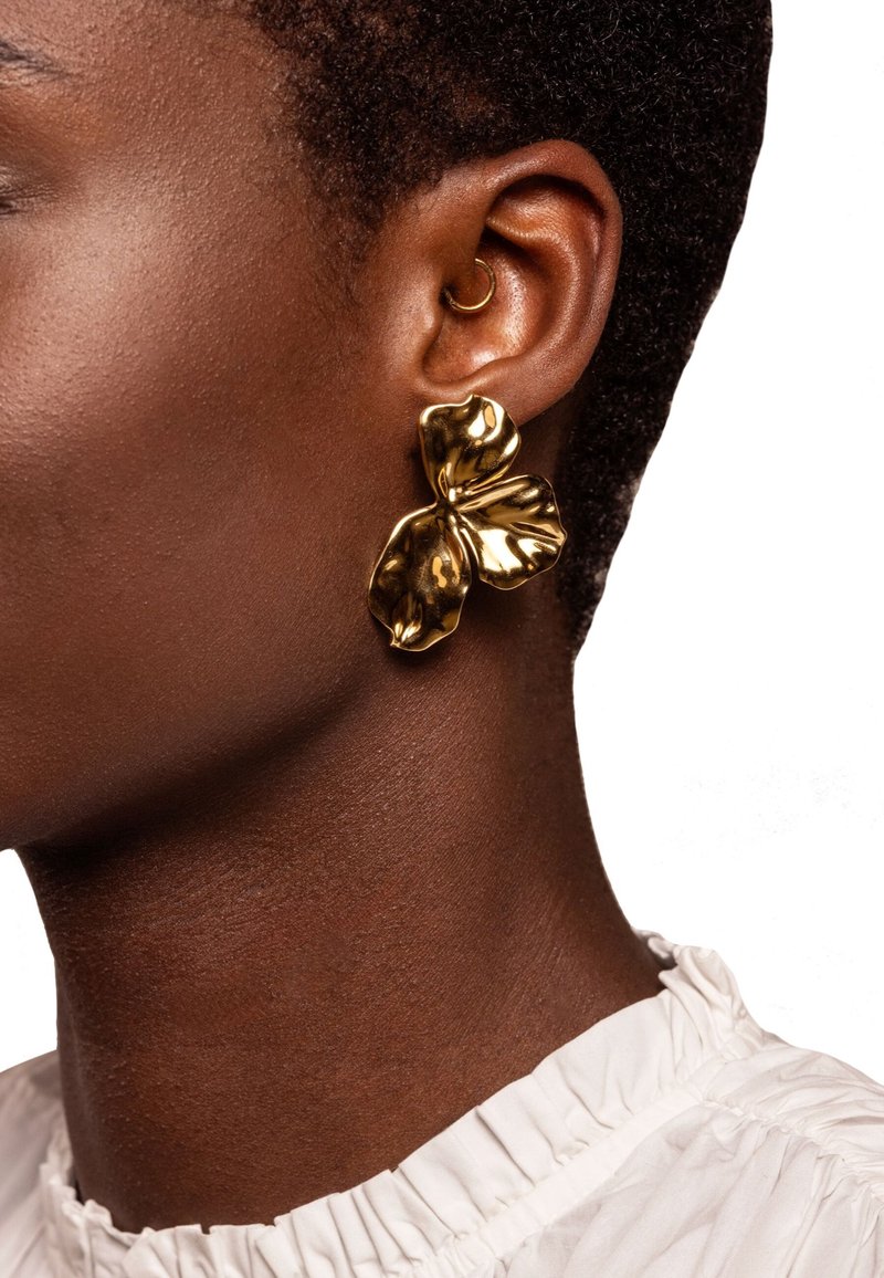 Close-up of a person wearing a large, shiny gold butterfly-shaped earring and a small gold hoop in the ear cartilage.