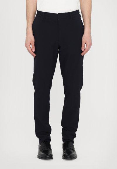 Pantaloni blu navy con un design aderente, vita elastica e tasche laterali. Realizzati in un tessuto morbido e testurizzato. Abbinati a scarpe nere.
