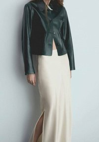 Černá kožená zkrácená bunda s knoflíkovým zapínáním a širokým límcem, spárovaná s krémovou saténovou sukní s vysokým bočním rozparkem.