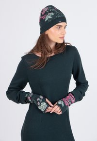 Pletená čiapka s kvetinovými vzormi v ružovej a zelenej farbe na tmavom pozadí, v kombinácii s topom s dlhým rukávom, ktorý má zladené kvetinové akcenty na manžetách.