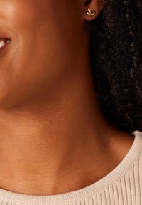 Gouden bladvormige studoorbellen op een persoon met een donkere huid, met een gestructureerd oppervlak en fijne details, zichtbaar tegen de gladde huid.