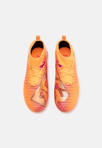 Jasnopomarańczowe buty sportowe o teksturowanej powierzchni, z różowymi akcentami i eleganckim designem. Posiadają wysoką cholewkę oraz wyraźne logo.