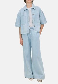 Helles blaufarbenes Denim-Jackett mit kurzen Ärmeln und zwei vorderen Taschen, kombiniert mit weitem, knöchellangem Hose mit Kordelzug aus passendem Material.