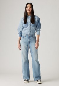 Light blue denim button-up shirt with two chest pockets, paired with high-waisted light blue wide-leg jeans and black and white sneakers.