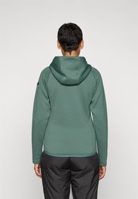 Grønn hettegenser laget av et teksturert stoff, med et tettsittende design, kontrasterende sømmer, og en kengurulomme foran.