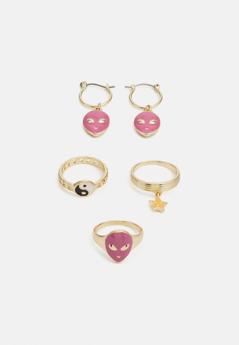 Conjunto de joias em tom dourado com argolas em forma de rosto alienígena rosa, um anel yin-yang e um anel com um encanto de estrela; acabamentos suaves e polidos.