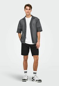 Grå t-shirt med korte ærmer og et mønstret tekstur, parret med sorte shorts. Hvid t-shirt under, sort-hvide sneakers, stribede sokker.