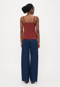 Bralett maroon dengan tali tipis dipadukan dengan celana denim biru lebar. Tekstur satin di bagian atas, denim yang kokoh dengan desain lima saku klasik.