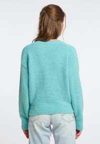 Maglione turchese lavorato a maglia con scollatura a girocollo, orlo a costine e spalle scese. Texture morbida e vestibilità rilassata, abbinato a jeans azzurri chiari.