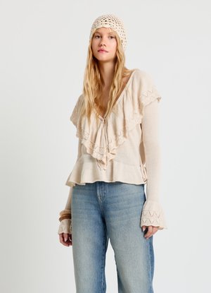 Haut en tricot crème avec un col à volants et un ourlet en crochet. Manches longues avec des poignets évasés. Associé à un jean bleu clair taille haute.