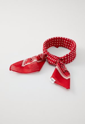 Czerwona materiałowa opaska na głowę w białe kropki zawiązana na supeł, z wzorzystymi trójkątnymi końcówkami i małą białą metką pielęgnacyjną.