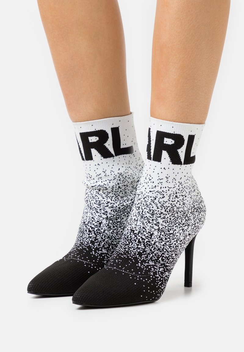 Bottes chaussettes en maille dégradé noir et blanc avec bouts pointus et talons aiguilles, ornées de lettres noires audacieuses près du haut du revers.