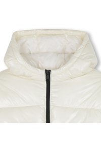 Luftig hvit jakke med quiltet mønster, høy krage og svart glidelåssdetalj. Jevn overflate med blank tekstur.