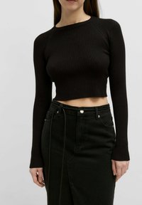 Zwarte geribbelde crop top met lange mouwen, ronde halslijn en getailleerd design, gecombineerd met een hoge taille zwarte denim rok met voorzakken.