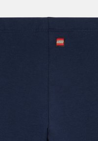 Dunkelblauter Stoff mit Mittelnaht und einem kleinen rechteckigen roten LEGO-Logo-Tag, das nahe der oberen Kante angenäht ist.