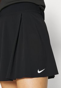 Mustat laskostetut urheiluhameet, jotka on valmistettu kevyestä kankaasta. Hameessa on sileä vyötärö ja erottuva valkoinen Nike-logo vasemmassa alakulmassa.