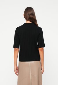 Zwart, kortemouwen gebreid shirt met verticale ribbels, ronde hals en een aansluitende pasvorm, gecombineerd met een gladde lichtbruine rok.