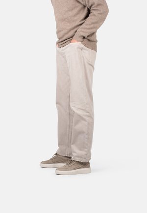 Pantalones de algodón beige con corte recto, que cuentan con bolsillos laterales y un acabado texturizado, combinados con zapatillas de deporte marrón claro.
