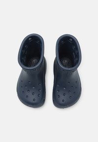 Une paire de bottes en caoutchouc bleu marine mi-mollet avec des trous de ventilation sur le dessus et les côtés, vues de dessus sur un fond blanc.