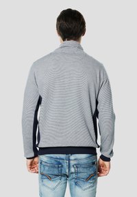 Jersey de cuello alto en gris y azul marino, con textura acanalada y diseño ajustado. Presenta paneles laterales en contraste y puños elásticos.