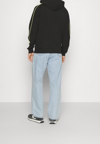 Svart huvtröja med gula sidostråk, kombinerad med ljusblå denimjeans och svarta sneakers. Slät textur, avslappnad passform.