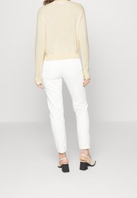 Pull crème avec ourlet côtelé, porté sur un pantalon blanc slim-fit. Les chaussures présentent des brides légères et un talon bloc noir. Pas de motifs visibles.