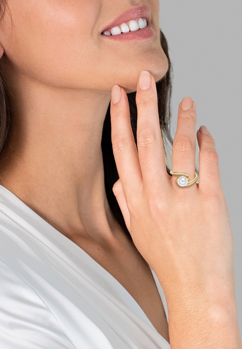 Zlati prstan z spiralo, okrašen s središnjo belo biserno, na teksturiranem kovinskem traku.